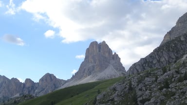 A mountain landscape with rocky peaks and green slopes under a partly cloudy sky.