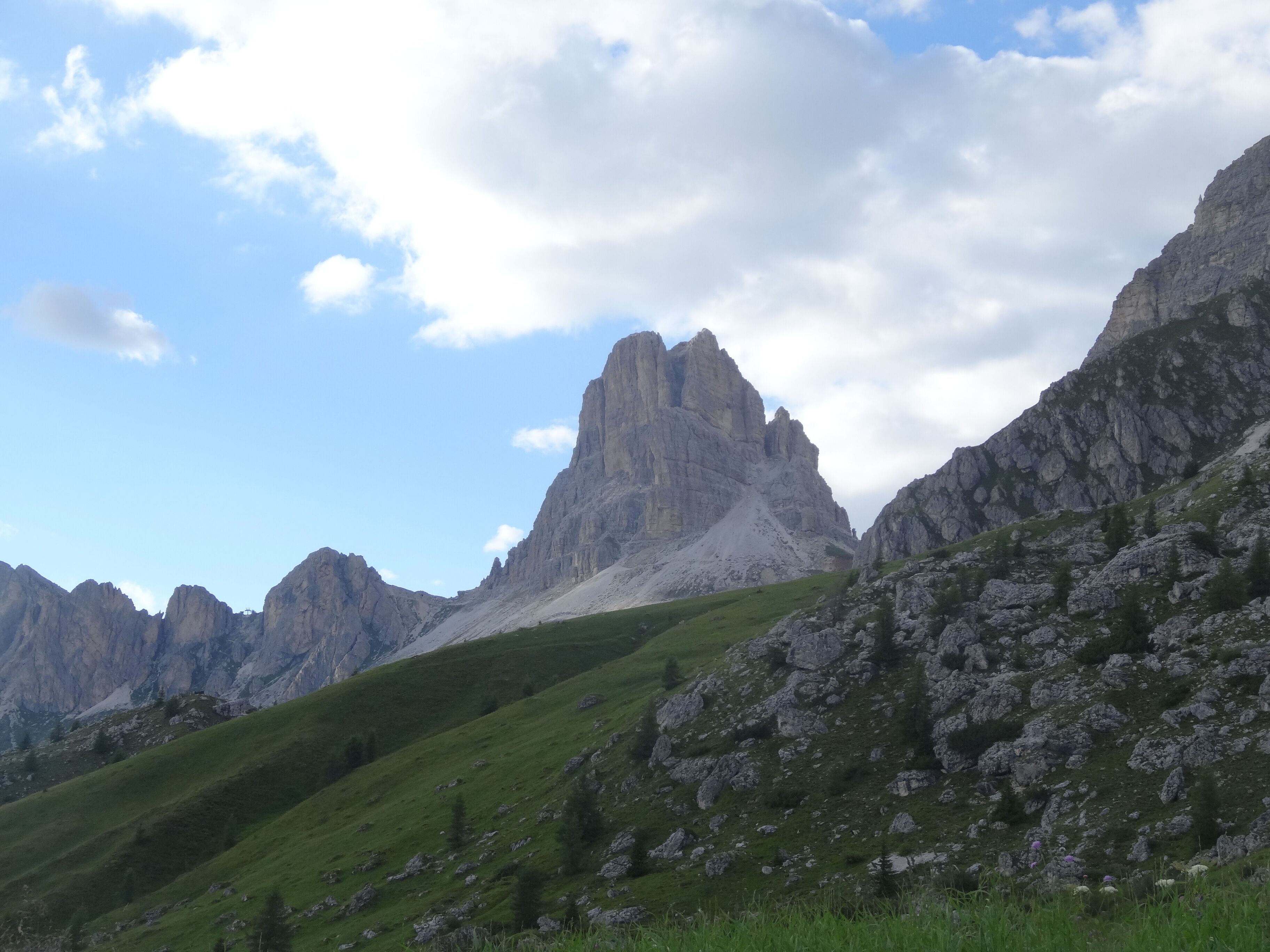 A mountain landscape with rocky peaks and green slopes under a partly cloudy sky.
