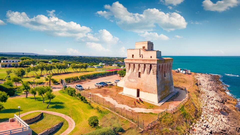 A coastal tower, a grassy area, and a rocky shoreline.