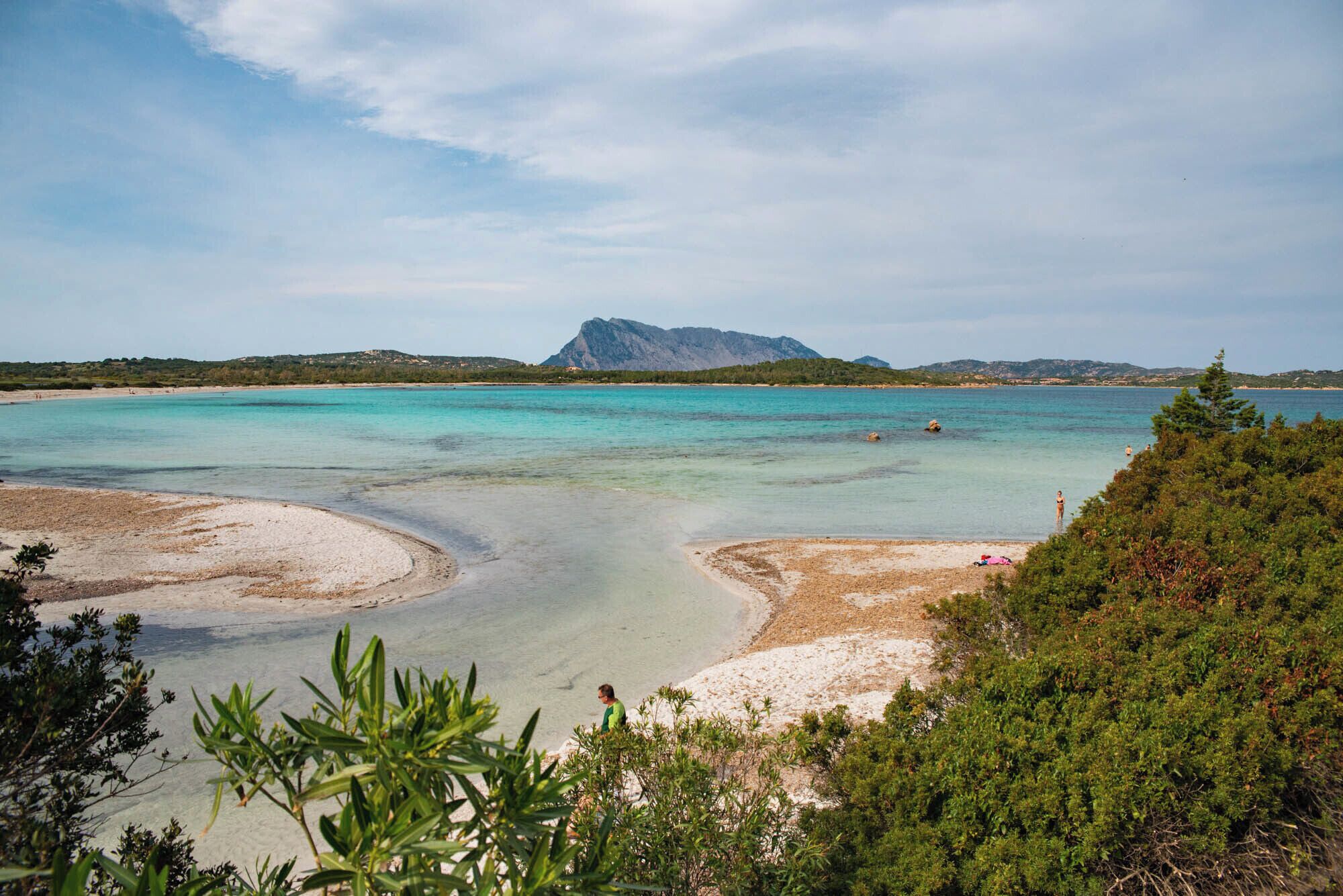 A coastal landscape with clear turquoise waters, sandy beaches, and a prominent mountain in the background.