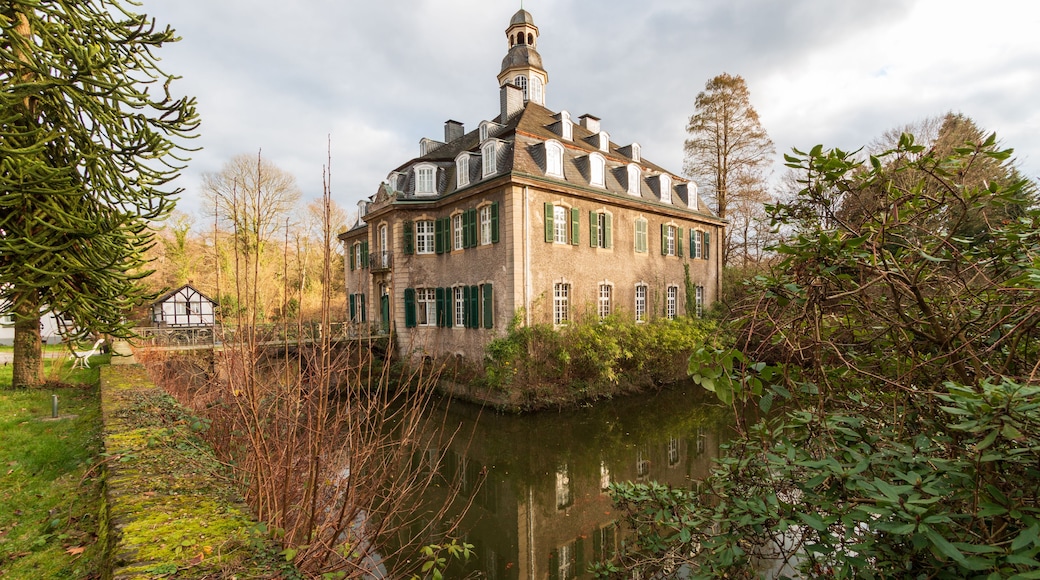 Un edificio histórico con una torre, rodeado por un río y abundante vegetación.