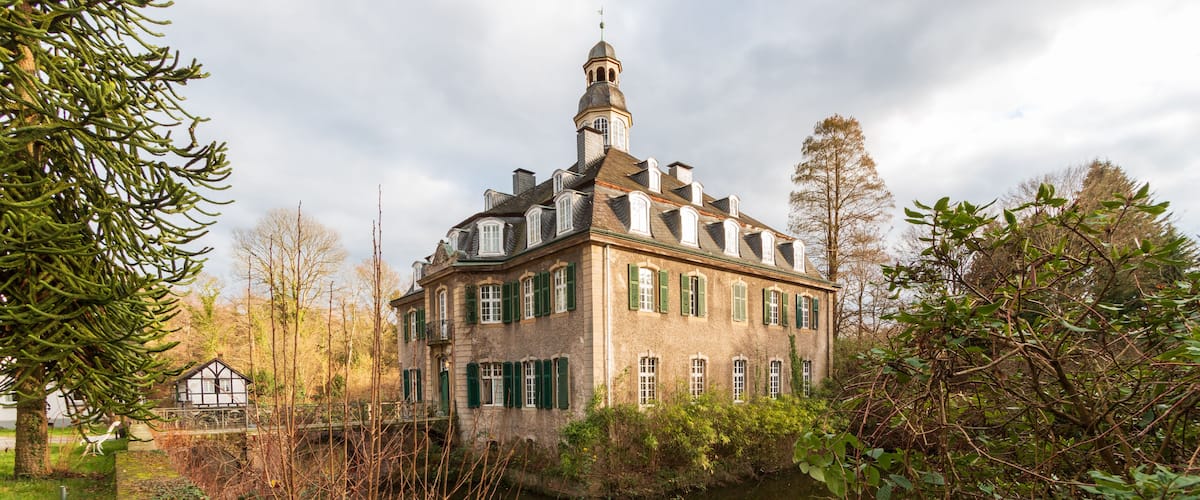 Ein historisches Gebäude mit einem Turm, umgeben von einem Fluss und üppiger Vegetation.