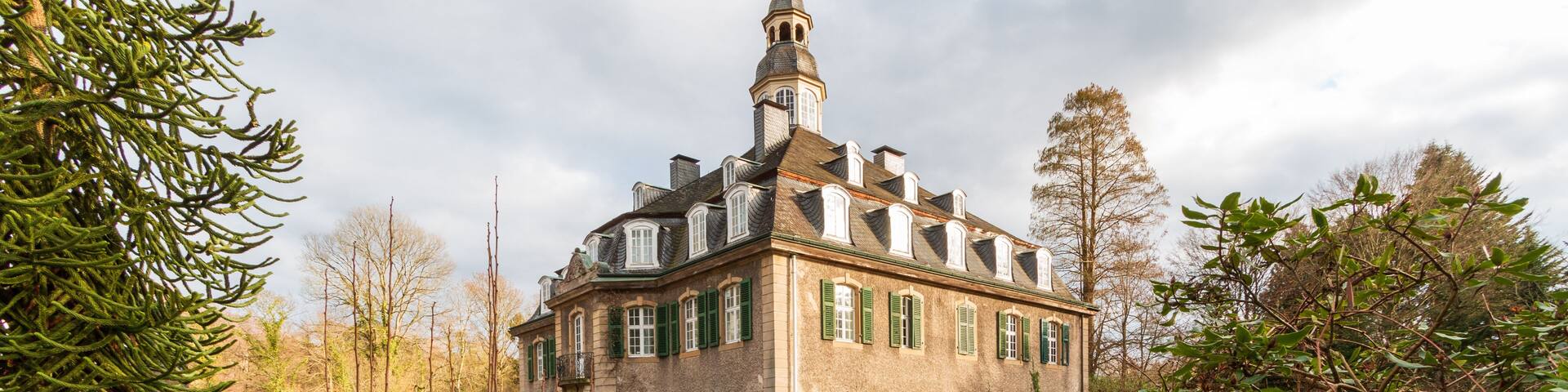 A historic building with a tower, surrounded by a river and lush greenery.