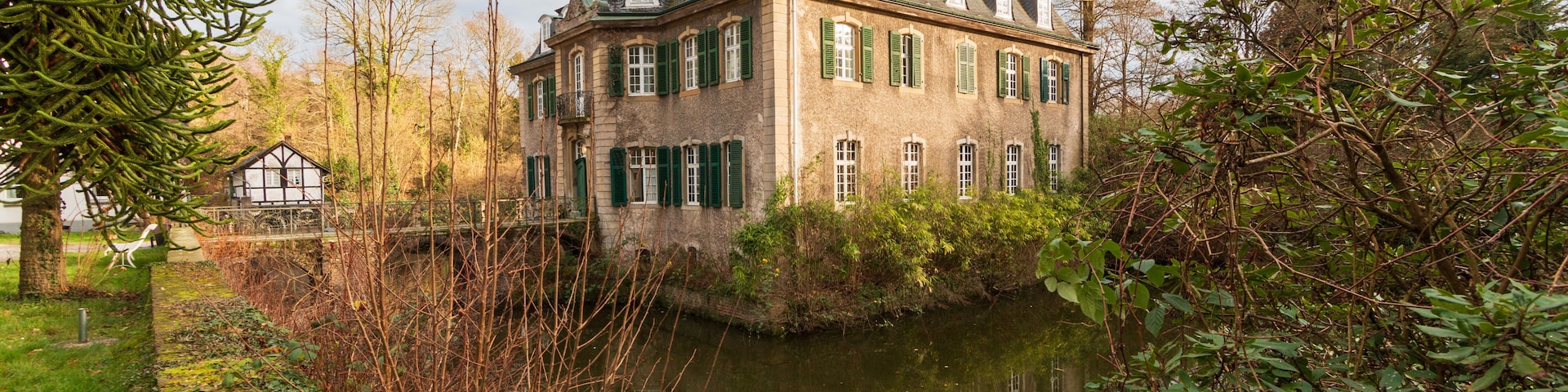 Um edifício histórico com uma torre, rodeado por um rio e vegetação exuberante.