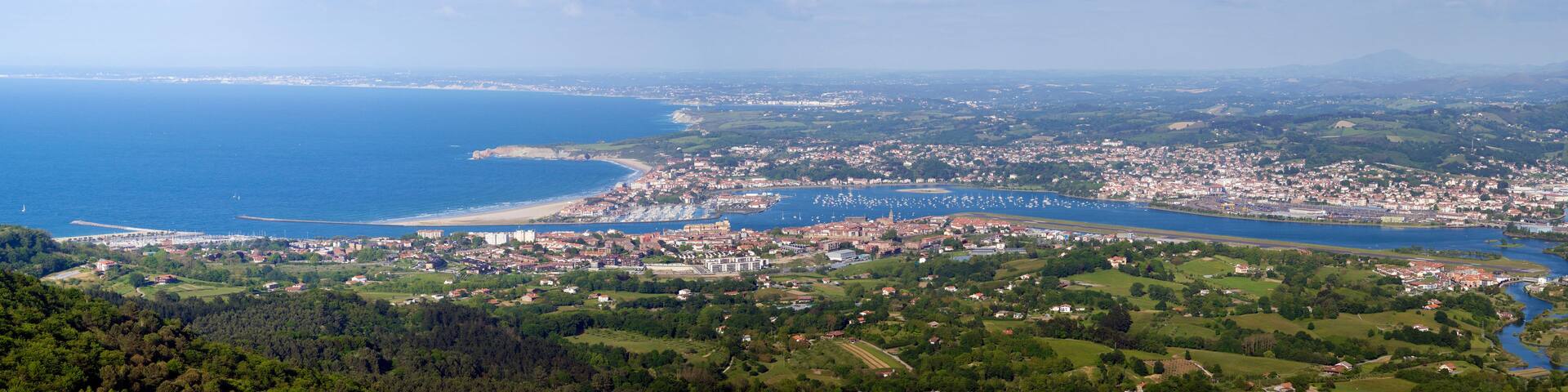 A coastal city with a bay, dense urban area, and surrounding green hills.