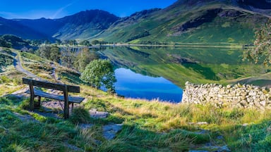A tranquil lake surrounded by mountains, a wooden bench, and a stone wall.