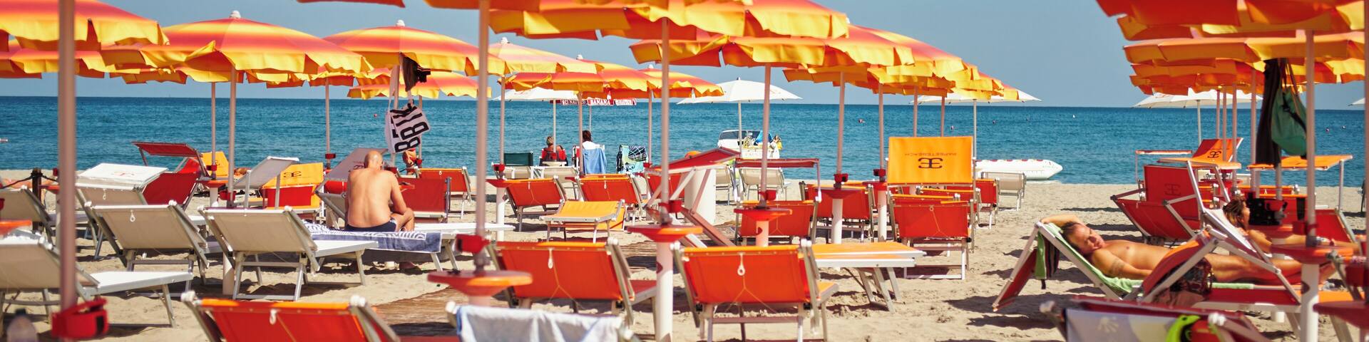 Una playa con hileras de sombrillas rojas y amarillas y tumbonas.