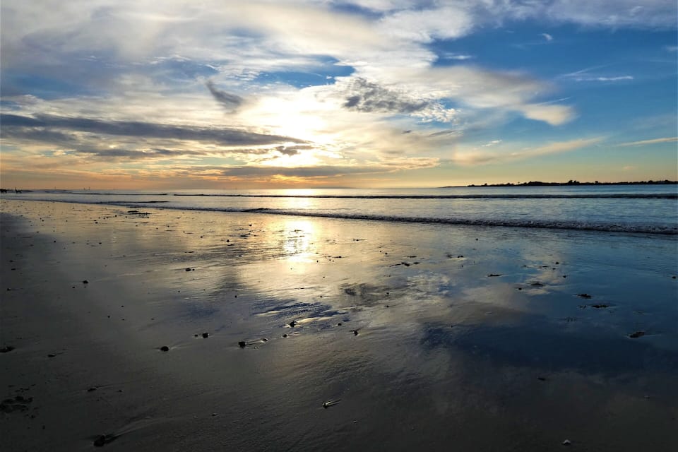 A beach at sunset with wet sand and a calm sea.