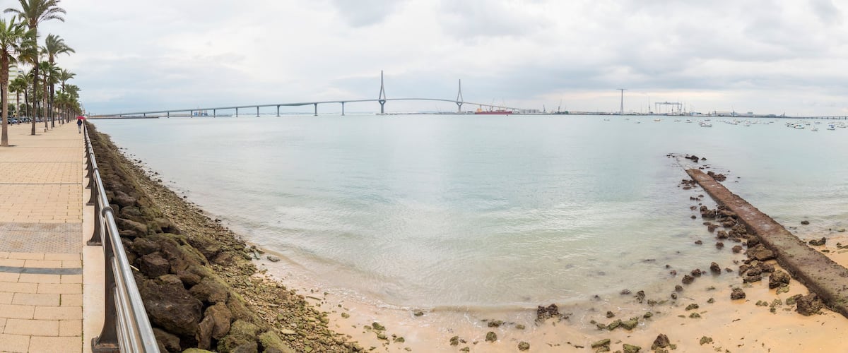 Un paysage côtier avec un pont, des bateaux et une plage de sable.