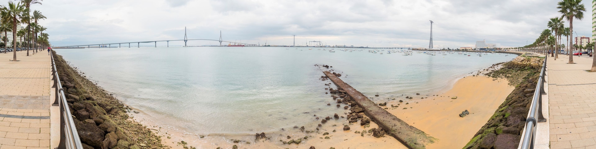 Paisagem costeira com uma ponte, barcos e uma praia de areia.