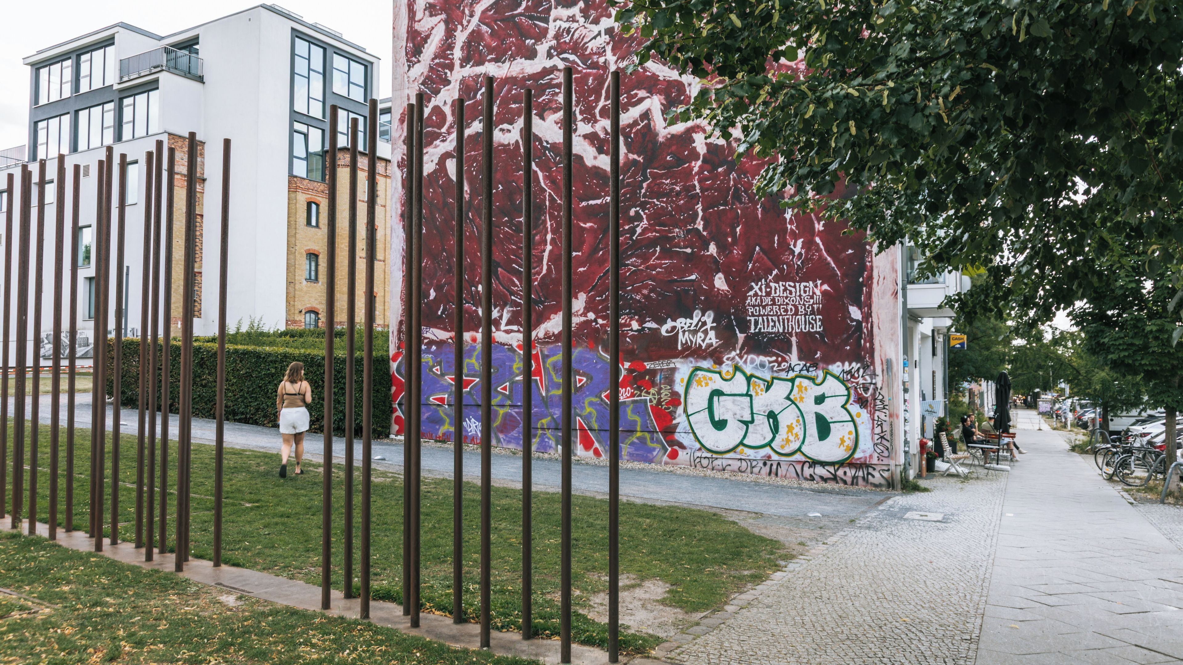 Une rue bordée d’un grand mur couvert de graffitis, de poteaux métalliques et d’un trottoir.