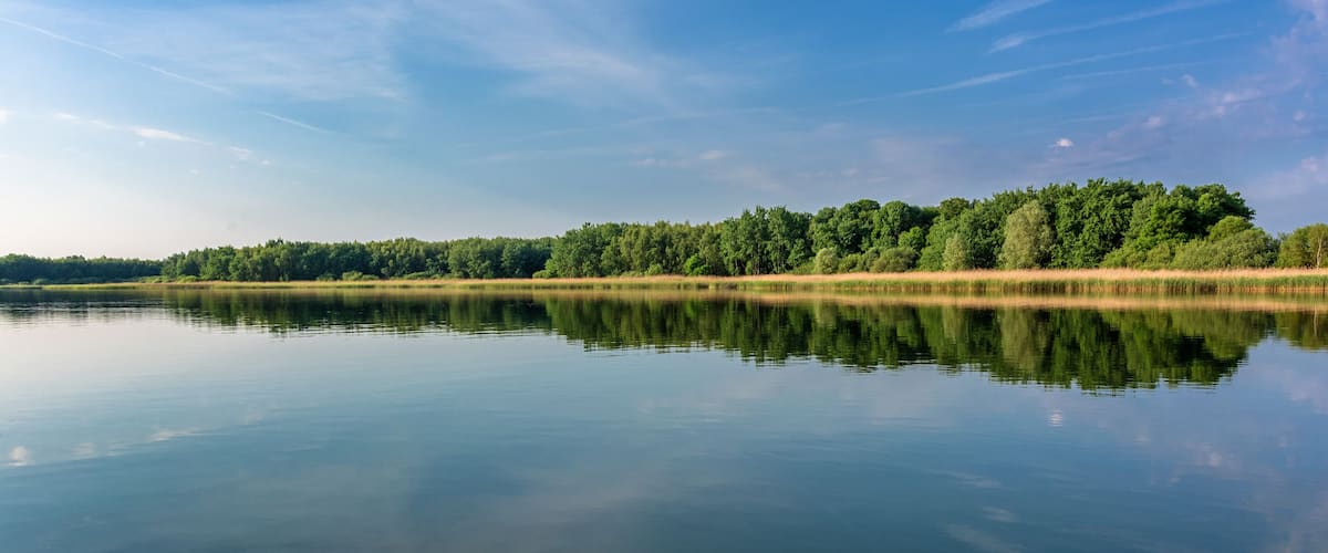 A calm lake with a clear reflection of the sky and trees.