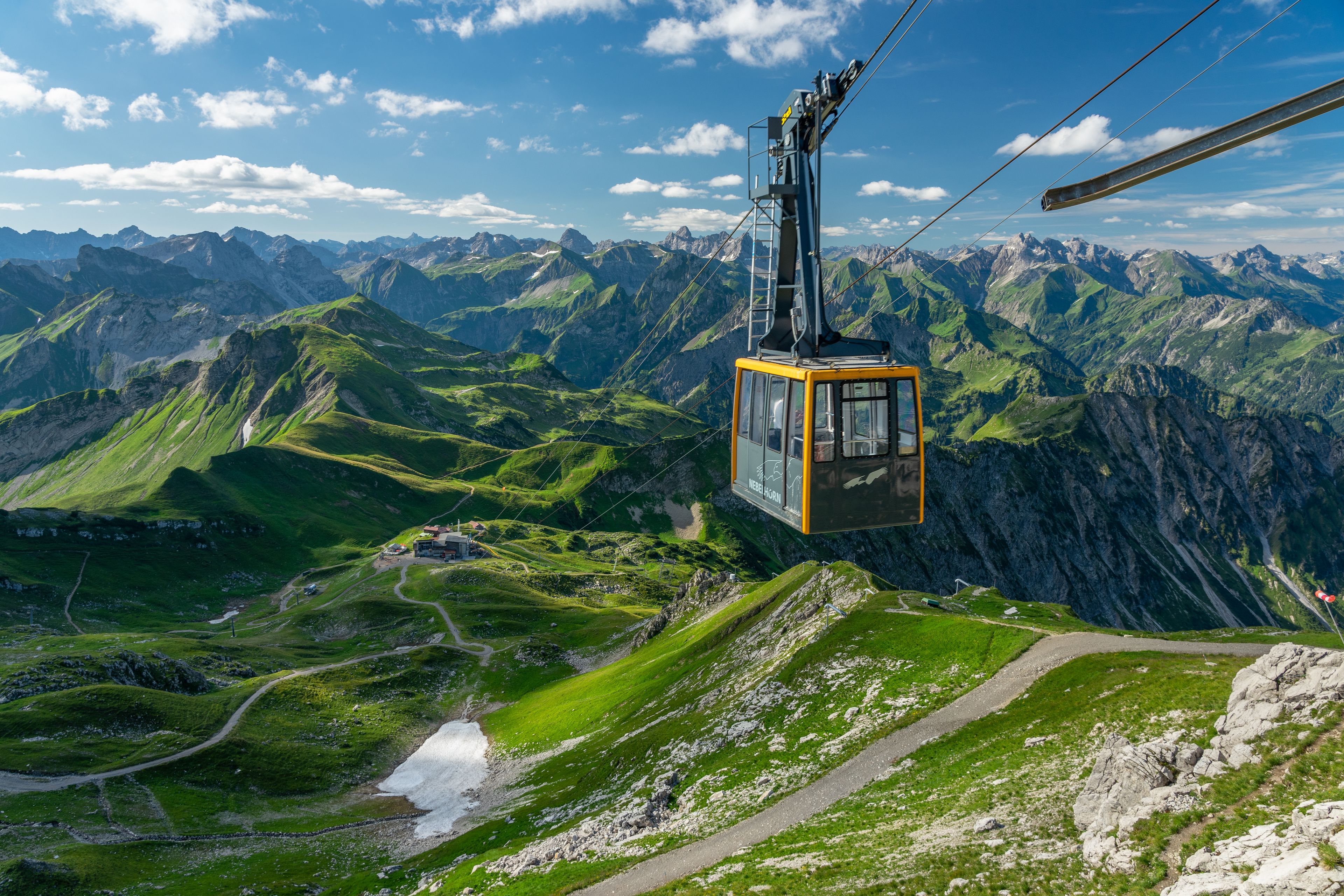 A cable car suspended over a mountainous landscape with green valleys and rocky peaks.