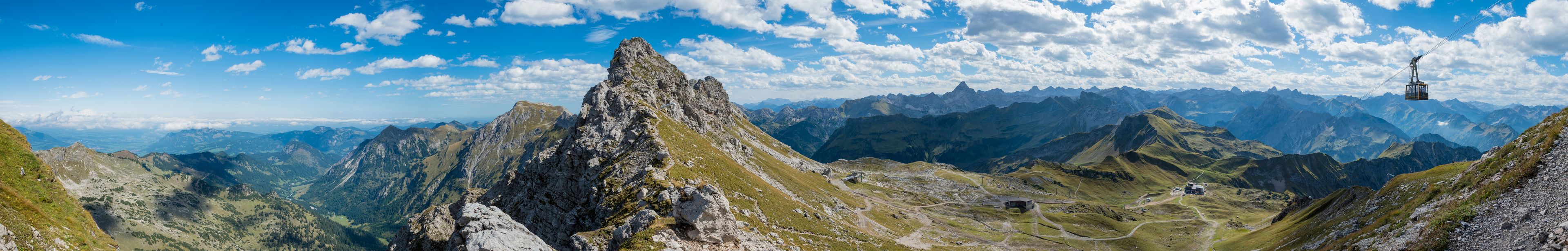 A mountain landscape with a prominent rocky peak, a cable car, and a winding road.