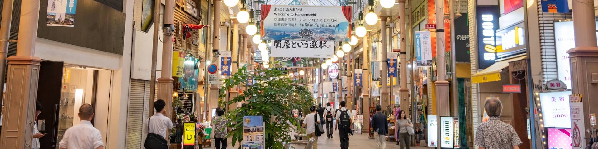 A covered shopping street with hanging signs and a central plant.