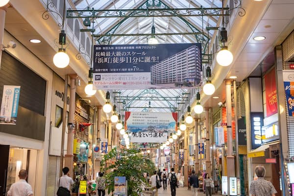 A covered shopping street with hanging signs and a central plant.