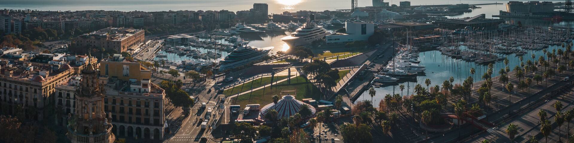 Aerial view of city port in Barcelona; parking for large luxury yachts in touristic capital of Catalonia; sunny day in Barcelonetta, sailboats, hotels, old buildinags illuminated by warm morning sun