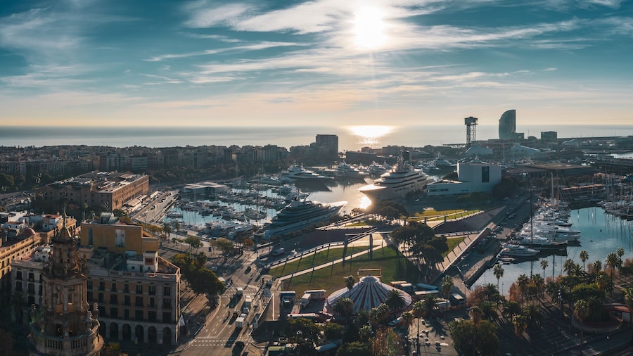 Aerial view of city port in Barcelona; parking for large luxury yachts in touristic capital of Catalonia; sunny day in Barcelonetta, sailboats, hotels, old buildinags illuminated by warm morning sun