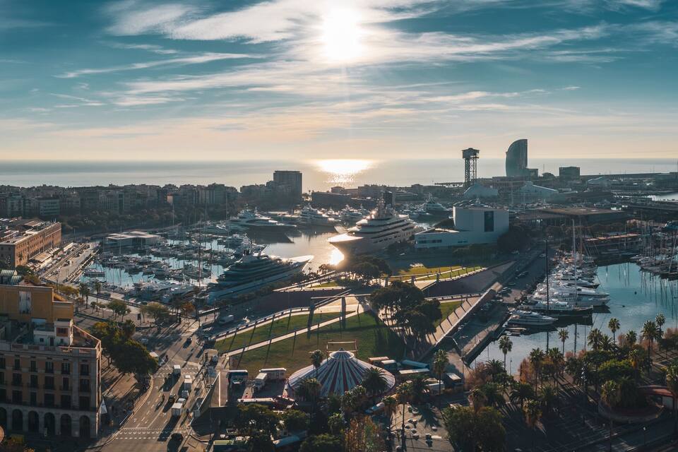 Un puerto deportivo con numerosos barcos, un río y un paisaje urbano con edificios y palmeras.