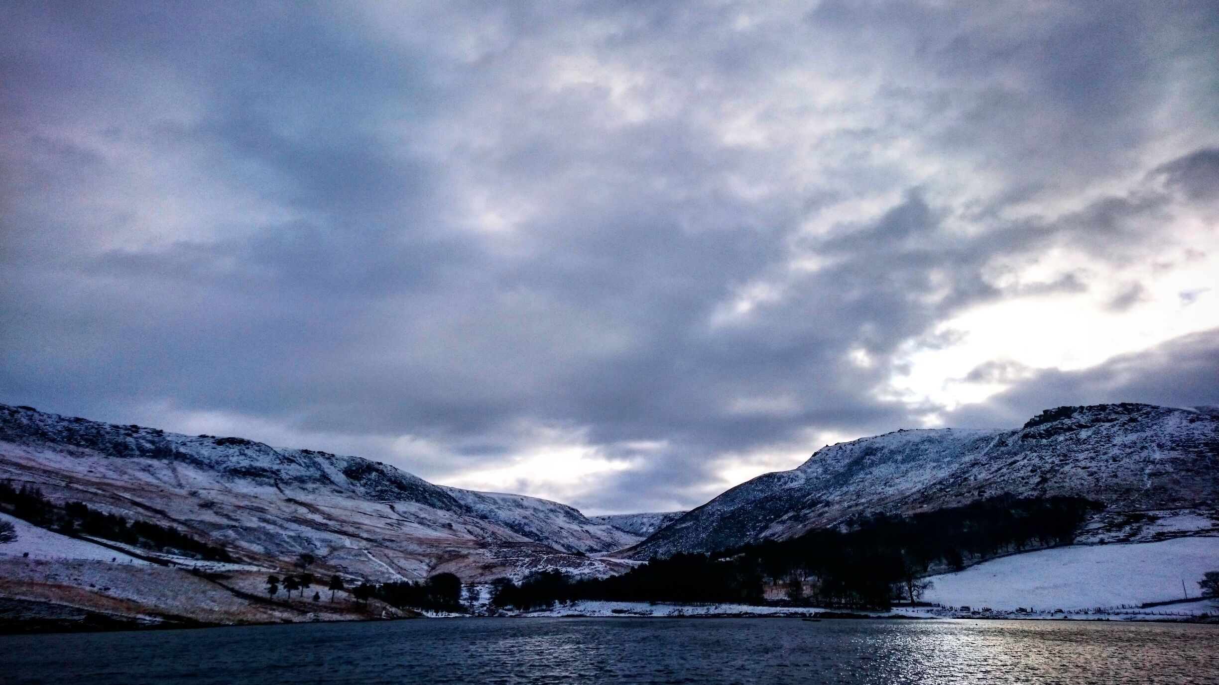 A snow-covered valley with a lake and mountains under a cloudy sky.