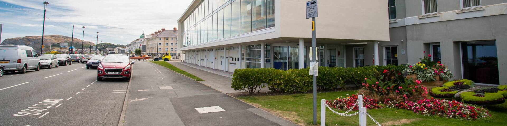 A modern building with a sign reading "Venue Cymru" and a parking sign nearby.