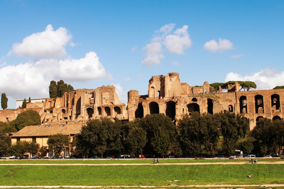 Ancient ruins with arches and columns, surrounded by green fields and trees.