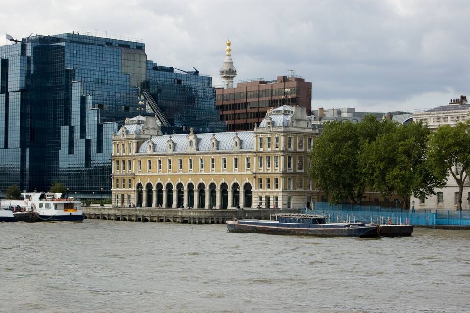 A historic building with arched windows and a dome, a modern glass skyscraper, and a river with boats.