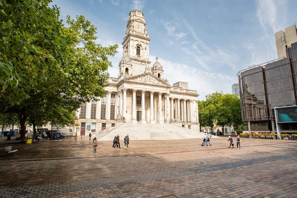 A historic building with a clock tower, surrounded by trees and a paved plaza.