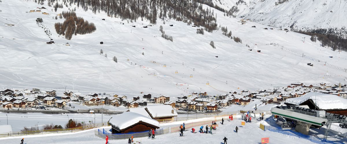 A snow-covered ski resort with ski lifts, a village, and mountains in the background.