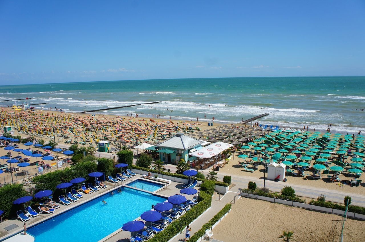 A beach resort with a swimming pool, beach umbrellas, and a lifeguard tower.
