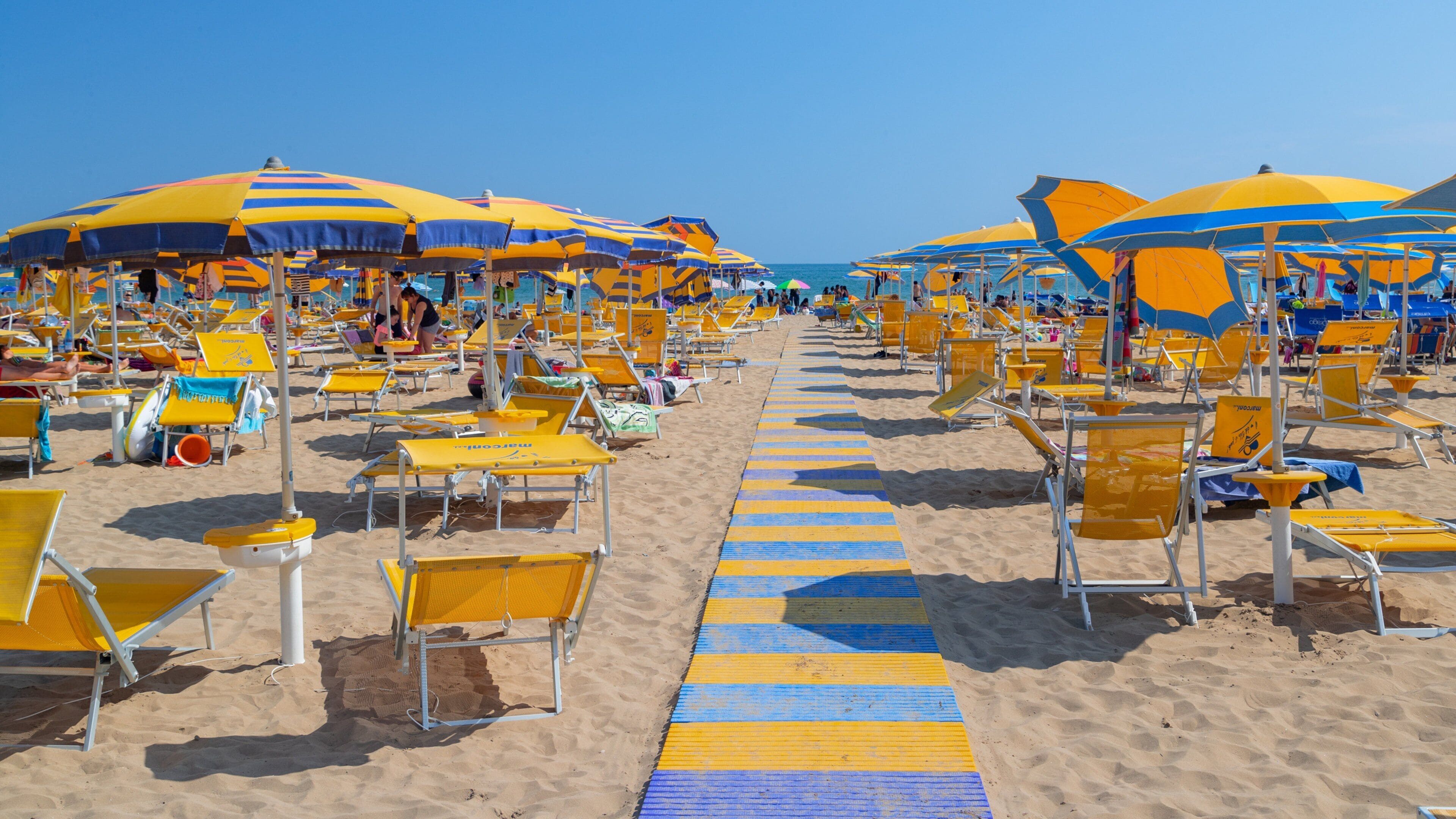 A beach with yellow and blue striped umbrellas and sun loungers.