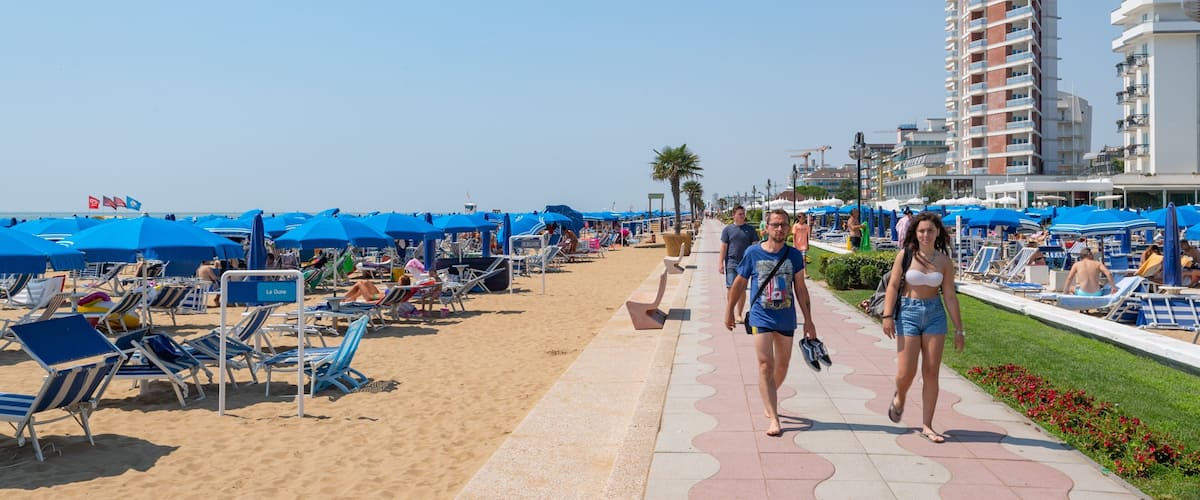 A beach with blue umbrellas, lounge chairs, and a tall building in the background.