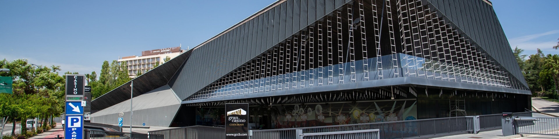 Un edificio moderno con un diseño triangular distintivo, un cartel de estacionamiento y una entrada con portón.