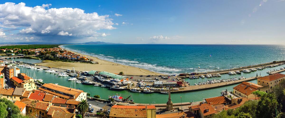 A coastal town with a marina, sandy beach, and a clear view of the sea.