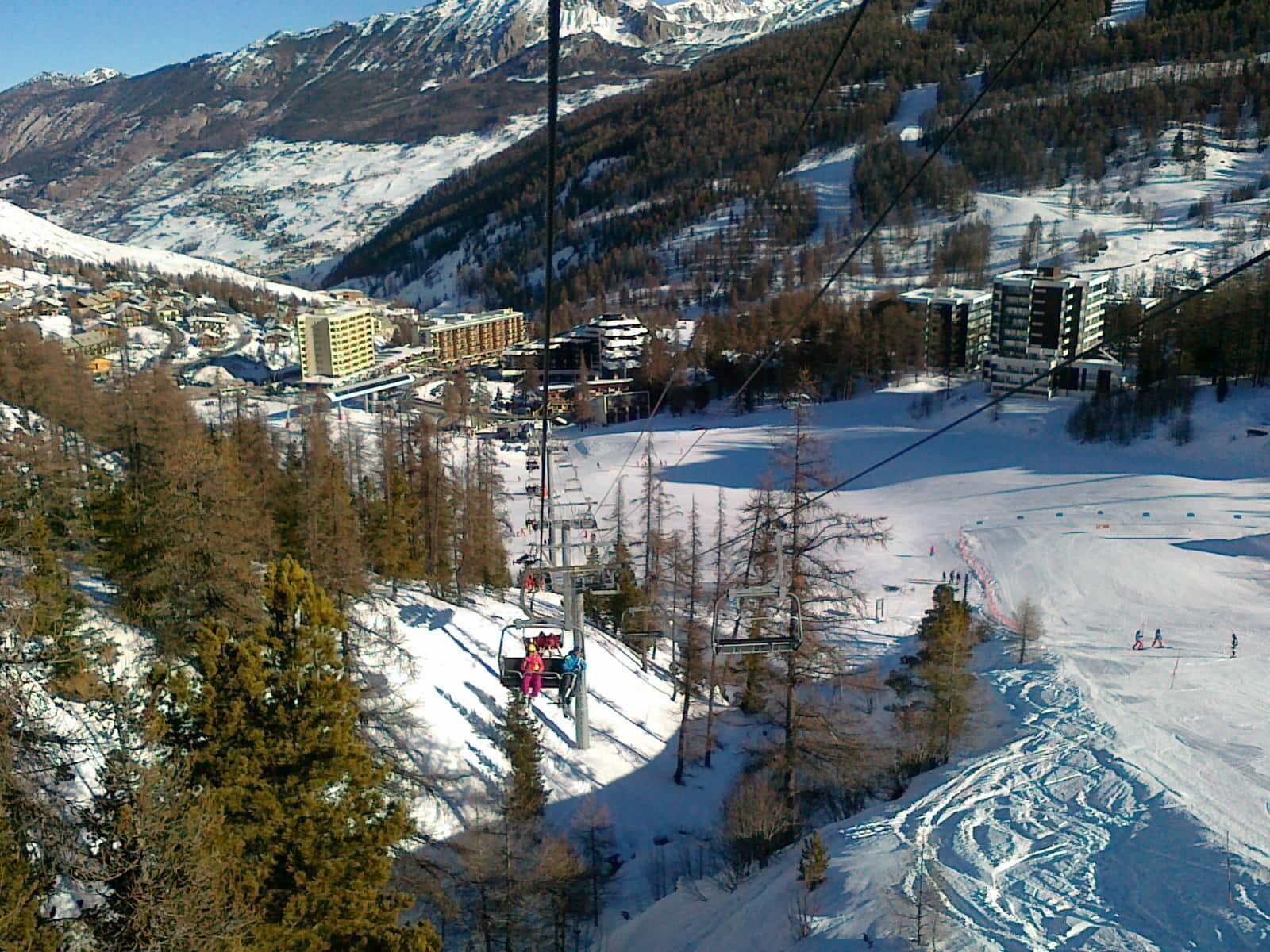 A snow-covered ski resort with ski lifts, buildings, and a mountainous backdrop.