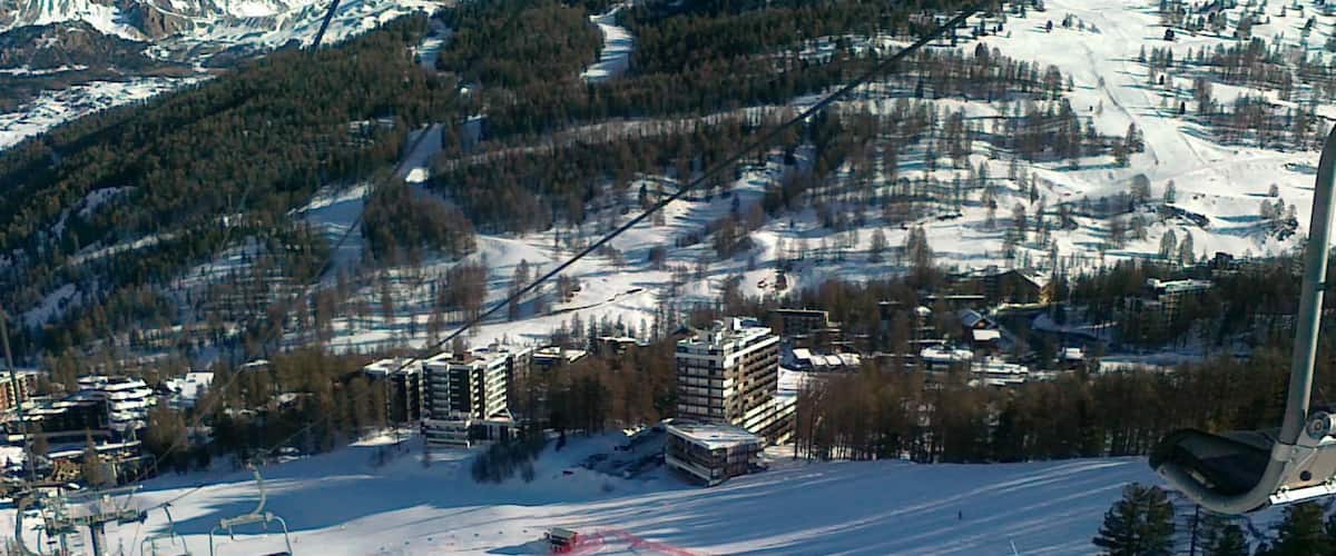 A ski slope with buildings and trees in the background.
