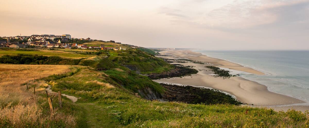 A coastal landscape with a sandy beach, grassy hills, and a distant town.