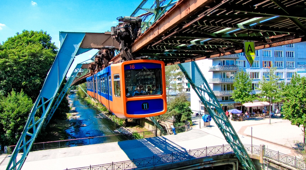 A blue and orange cable car crossing a bridge over a river, with buildings and trees in the background.