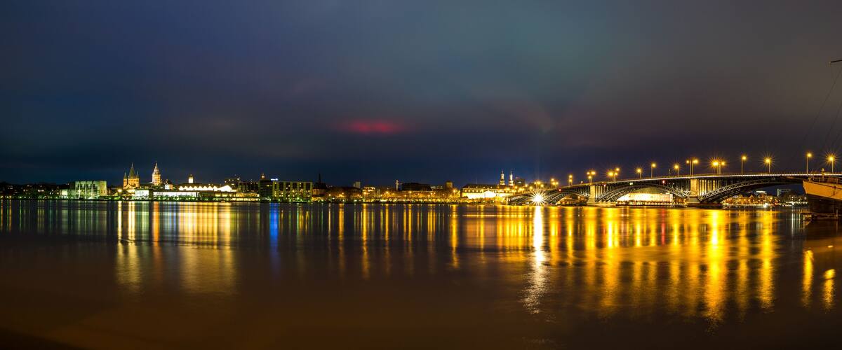 A nighttime river scene with a bridge, illuminated buildings, and a boat docked on the right.