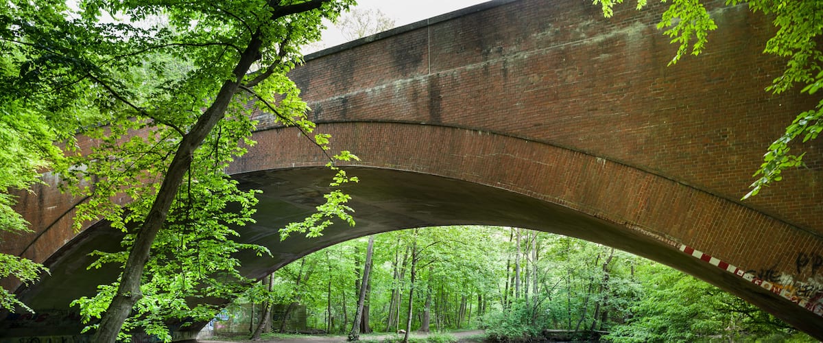 A brick bridge over a calm river, surrounded by lush greenery and trees.