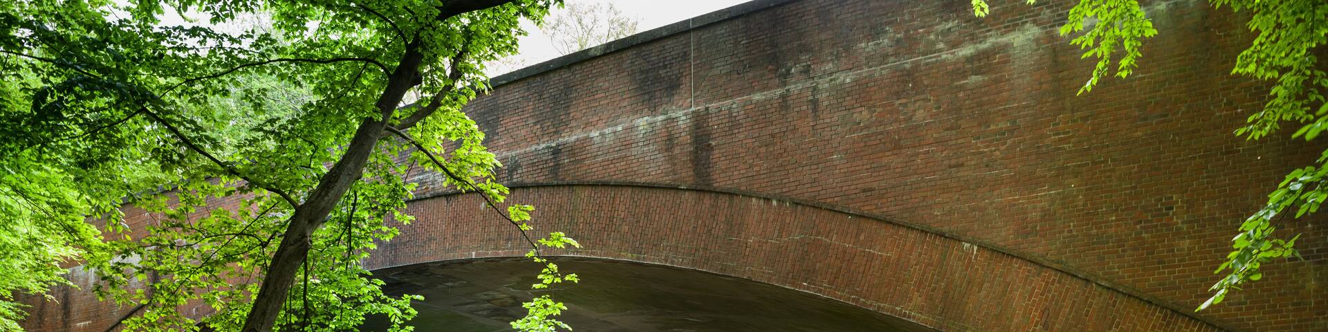 A brick bridge over a calm river, surrounded by lush greenery and trees.