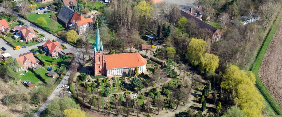 An aerial view of a town with a prominent church, surrounded by a cemetery and lush greenery.