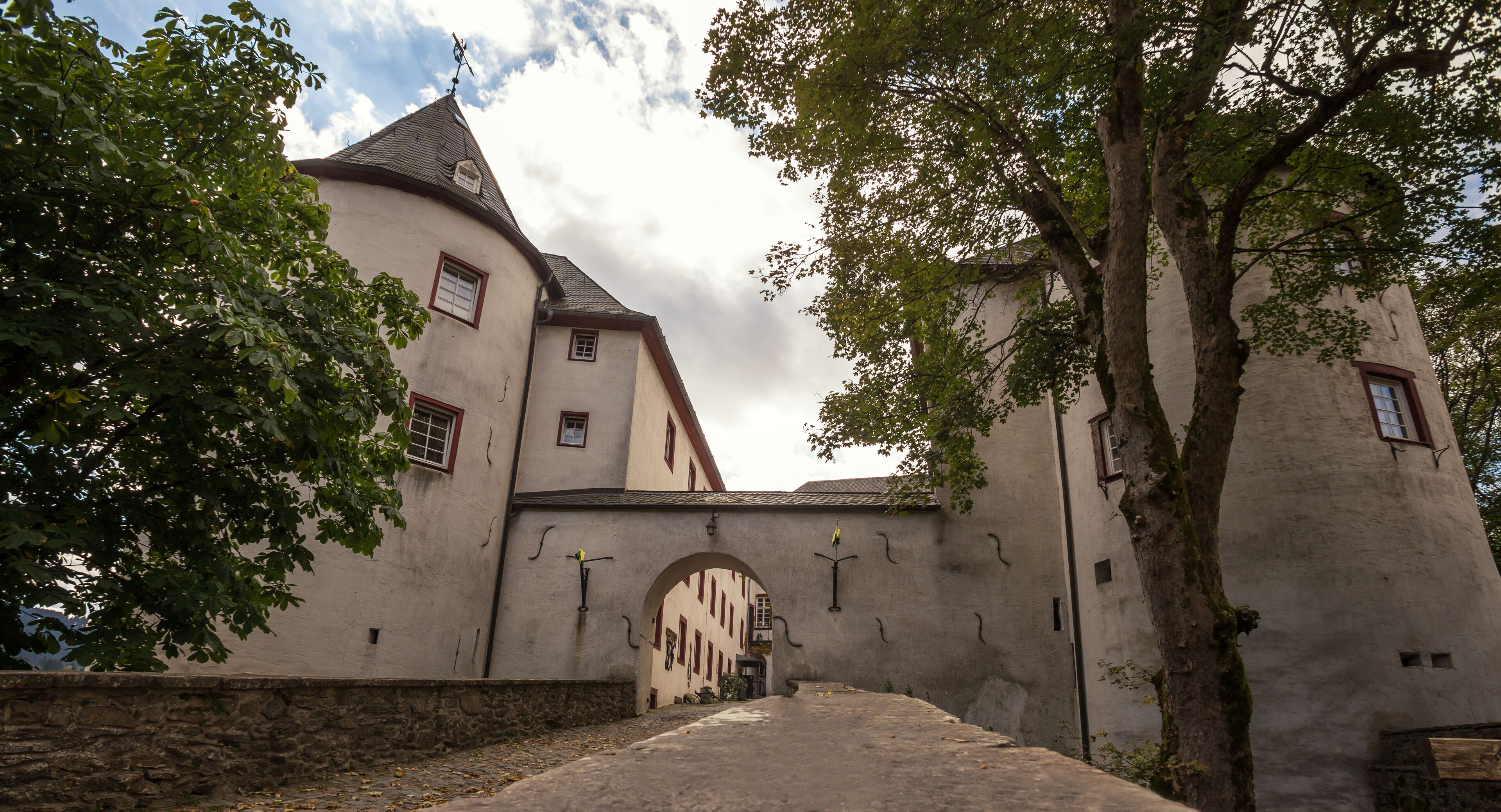 A historic building with a stone wall, a large tree, and a clear sky.