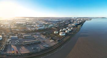 An aerial view of a large industrial complex with storage tanks, a railway, and a body of water.