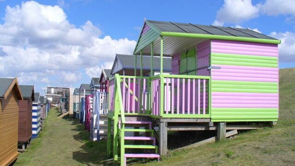 A row of colorful beach huts with a grassy path leading to them.