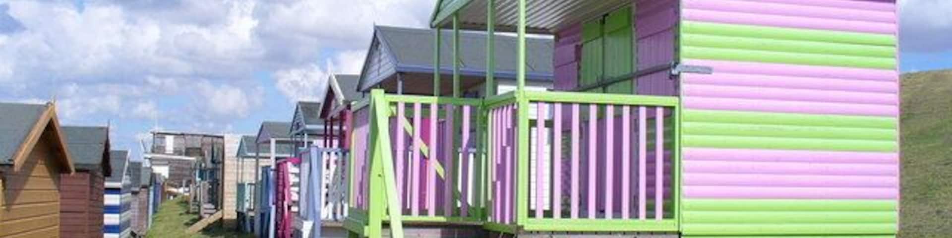 Beach Huts Alley Colourful rows of wooden huts with verandas on the grassy slopes below Marine Parade, Tankerton. In the distance is Tankerton Bay Yacht Club.