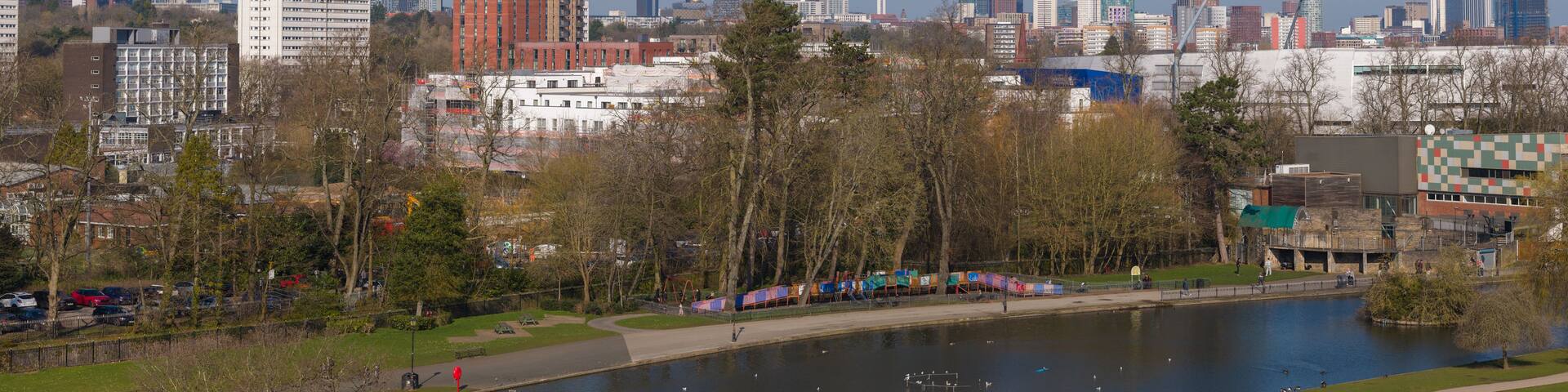 A river with ducks, a park with benches, and a city skyline in the background.