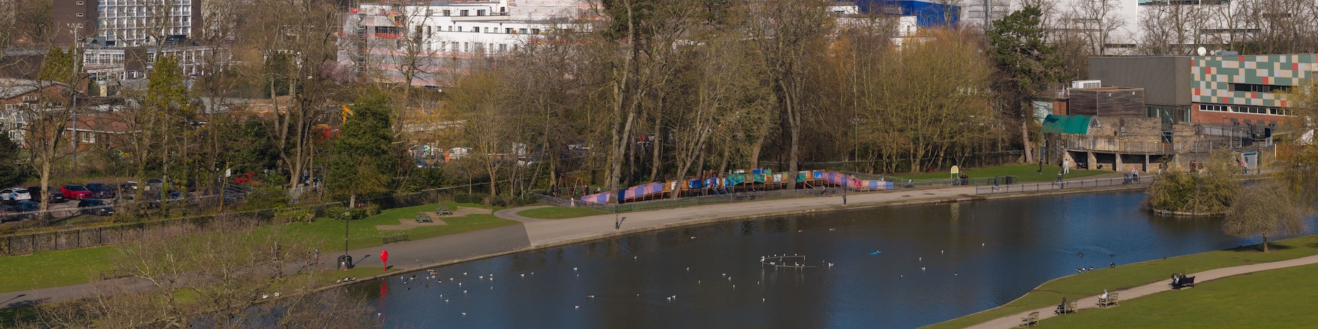 Une rivière où nagent des canards, un parc avec des bancs et, au loin, le panorama de la ville.