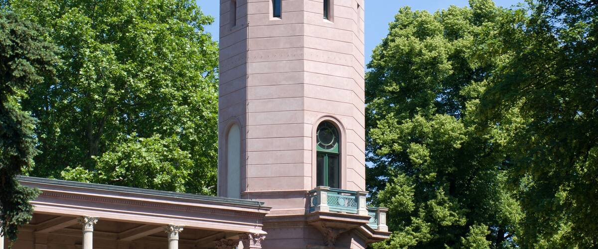Ein pinkfarbener Turm mit einer Kuppel und einer Flagge, umgeben von üppigem Grün.