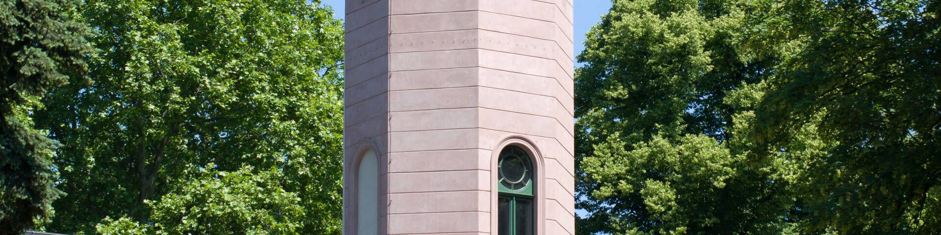 A pink tower with a dome and a flag, surrounded by lush green trees.